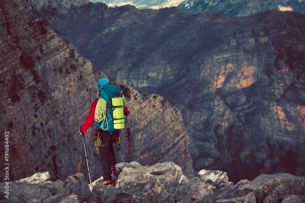 Young mountaineer standing with backpack on top of a mountain and enjoying the view