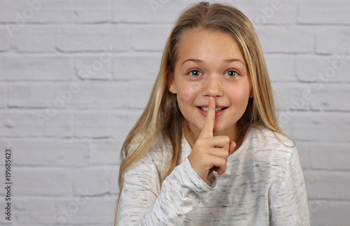 Portrait of happy smiling 10 years old kid girl showing silence gesture photo