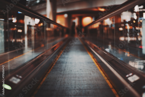 Shooting with shallow depth of field of moving walkway in modern airport terminal waiting hall; travelator trough departure area of railway station depot with multiple bokeh shapes around