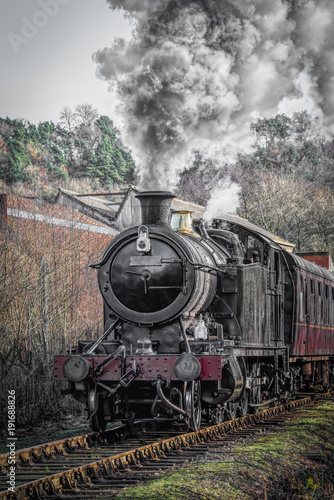 A upright vertical view of a steam train locomotive in motion facing forward and smoking