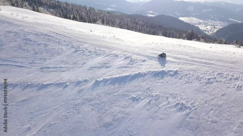 View from the height on people driving snowmobile on beautiful snowy mountain slope. Clear frosty weather View from the height on people driving snowmobile on beautiful snowy mountain slope. Clear frosty weather