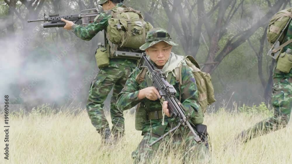 Squad of Fully Equipped and Armed Soldiers Moving Through Grass and Preparing to Fire. Squad Moving Behind Him. Squad of Fully Equipped and Armed Soldiers Moving Through Grass and Preparing to Fire. Squad Moving Behind Him.