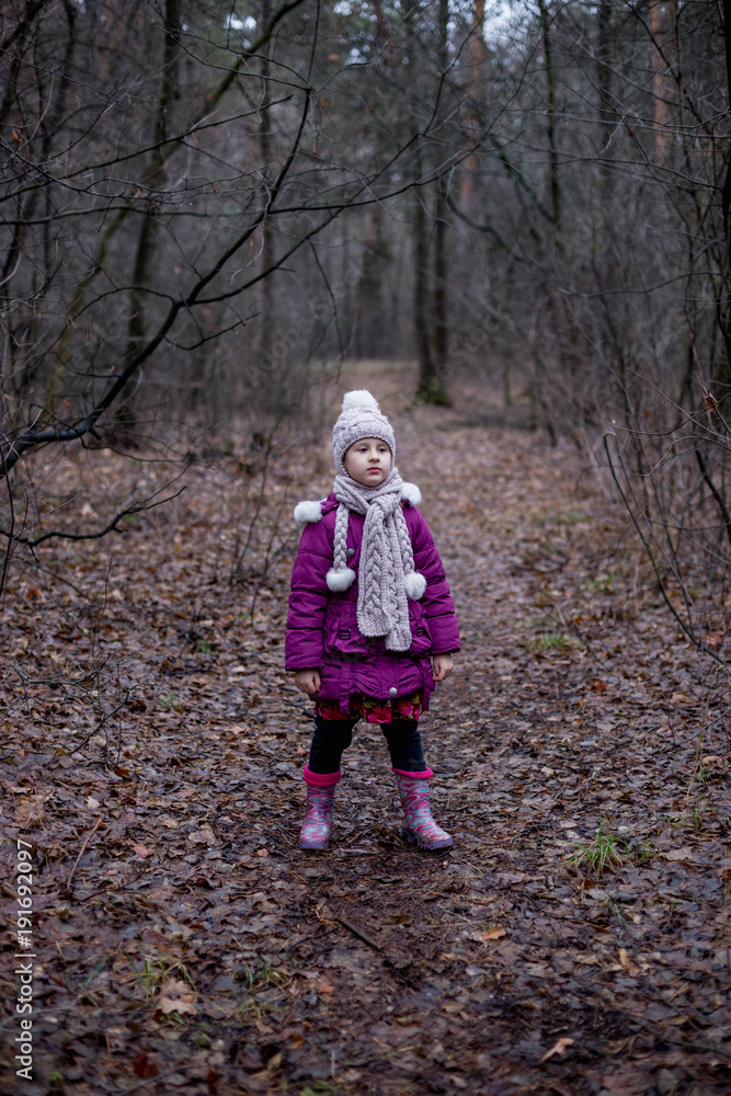 A little girl is standing in a forest on a path. A little girl is standing in a forest on a path.