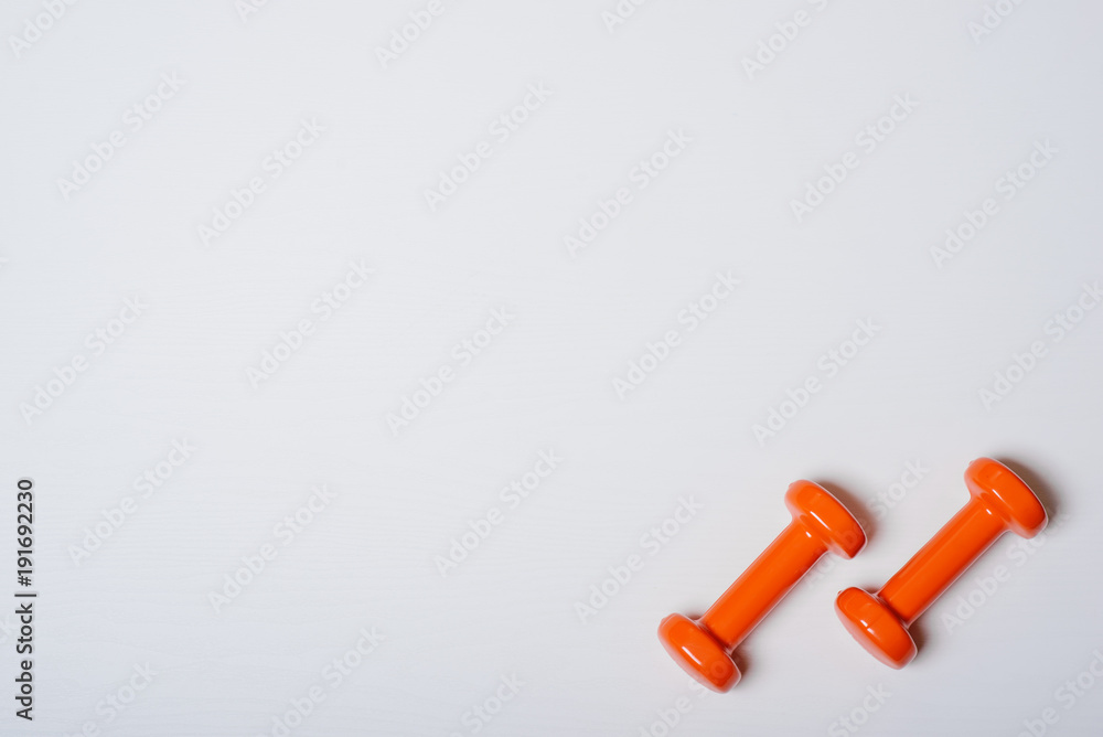 Two dumbbells of orange are lying on a white background with a tree texture