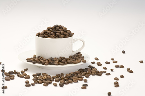 Coffee beans in a white cup and saucer on a plain background