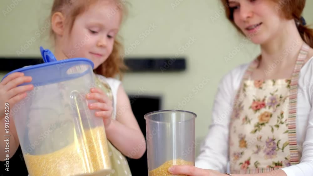 Young happy mother and her cute curly toddler daughterr in a kitchen to cook Young happy mother and her cute curly toddler daughterr in a kitchen to cook