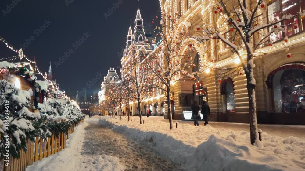 Beautiful Red Square New Year winter decorations, steady camera shot along night shining pedestrian street in the center of Moscow, trees with bright lights and balls are covered with snow.