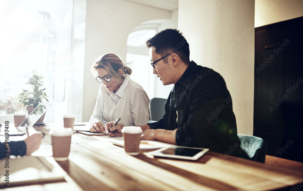 Diverse coworkers sitting at a table in an office Diverse coworkers sitting at a table in an office