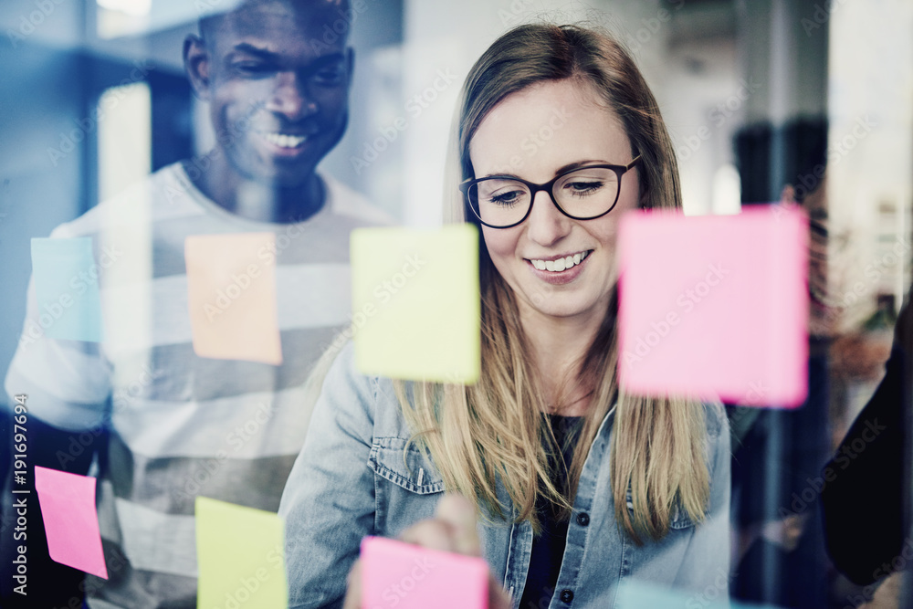 Diverse businesspeople brainstorming with sticky notes on a glass wall Diverse businesspeople brainstorming with sticky notes on a glass wall