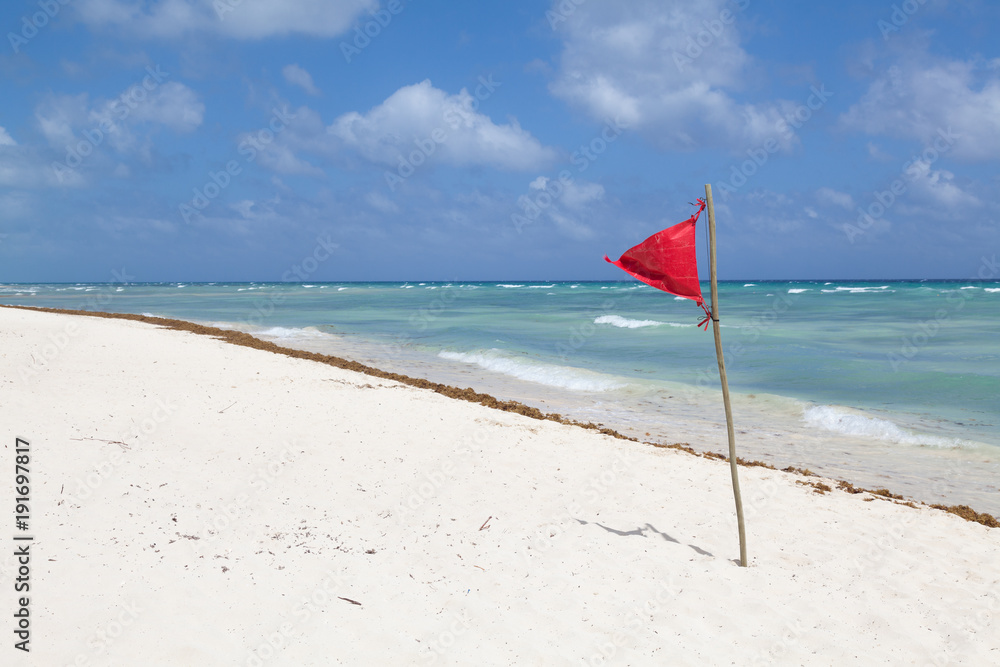 Red flag on a beach. Beautiful sea view, white sand, blue sky