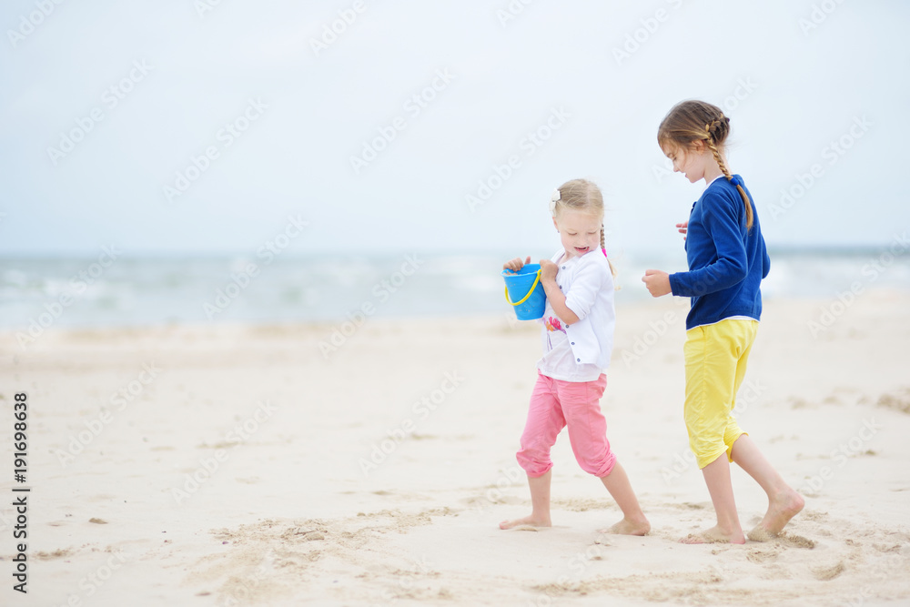Two little sisters having fun on a sandy beach on warm and sunny summer day. Kids playing by the ocean. Two little sisters having fun on a sandy beach on warm and sunny summer day. Kids playing by the ocean.