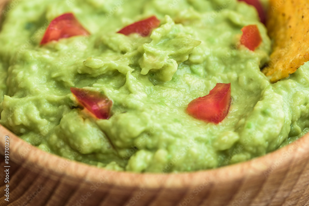 Close Up of Guacamole with Tortilla Chip in Wooden Bowl