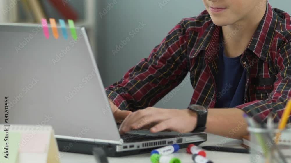 Teenage boy smiling and typing on laptop, doing homework, student workplace Teenage boy smiling and typing on laptop, doing homework, student workplace