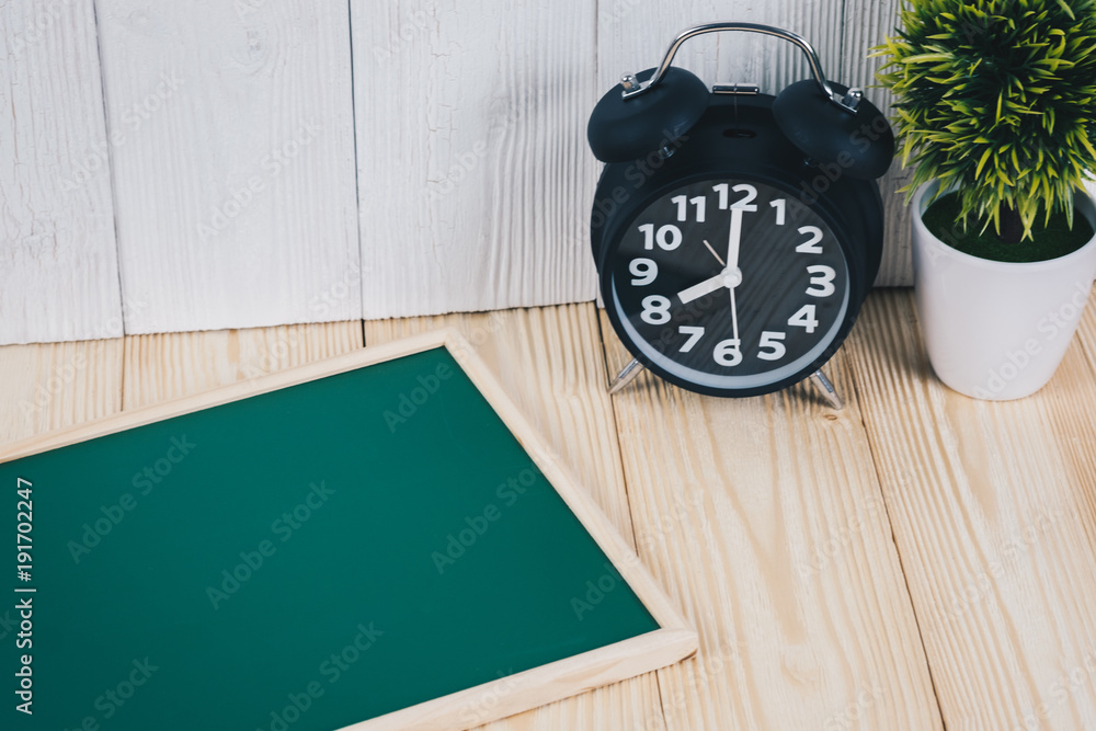 Blank green chalkborad with wood frame and little decorative tree in white vase and vintage alarm clock on wooden table with copy space. Blank green chalkborad with wood frame and little decorative tree in white vase and vintage alarm clock on wooden table with copy space.