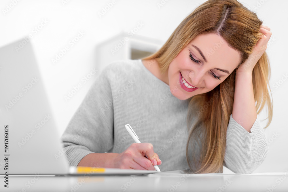 Attractive young woman in a good mood works with documents in the office or at home. Writes, fills papers at the desk with a laptop. Attractive young woman in a good mood works with documents in the office or at home. Writes, fills papers at the desk with a laptop.