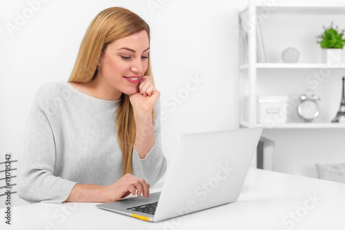 Attractive blond woman looking at laptop screen while sitting at desk in office or at home. © Denis Rozhnovsky