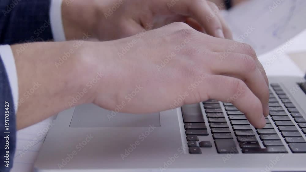 Close up of businessman hands are typing the data on laptop keyboard. Professional traider is pushing the bottons by his fingers and his female colleague, who is sitting near, checking rates on graph Close up of businessman hands are typing the data on laptop keyboard. Professional traider is pushing the bottons by his fingers and his female colleague, who is sitting near, checking rates on graph