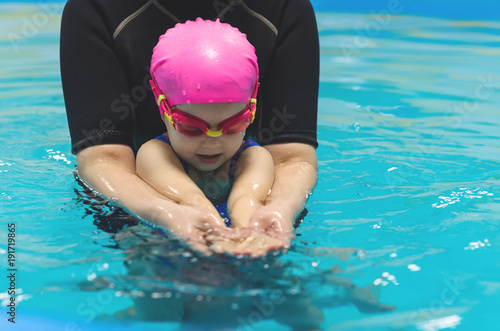 A little girl of European appearance in a pink rubber cap learning to swim in the pool