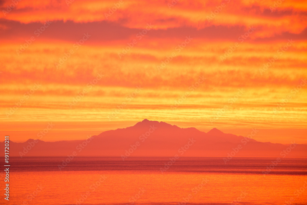 Vibrant orange ocean sunset with mountains