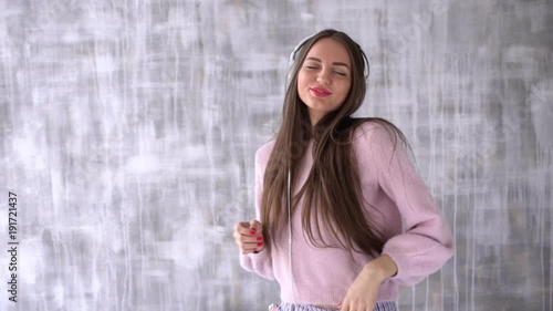 Girl loves music. A girl in headphones dancing on a light background using cell phone. slow-motion photo