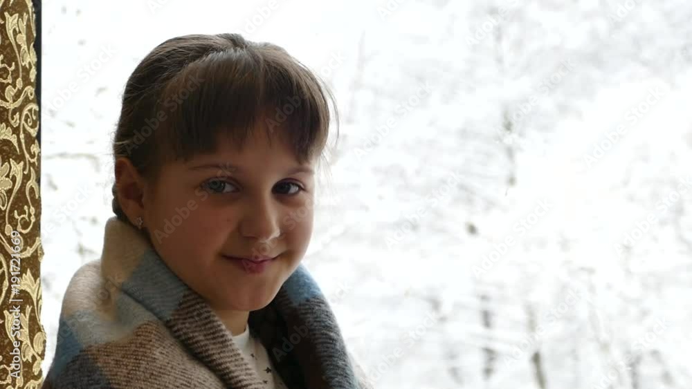 A girl in a plaid near the window in winter. Beautiful girl smiling. Outside the window is winter and trees in the snow. A girl in a plaid near the window in winter. Beautiful girl smiling. Outside the window is winter and trees in the snow.