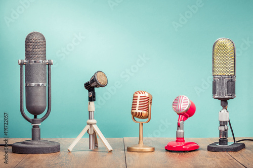 Retro old microphones for press conference or interview recording on wooden table front gradient aquamarine wall background. Vintage old style filtered photo