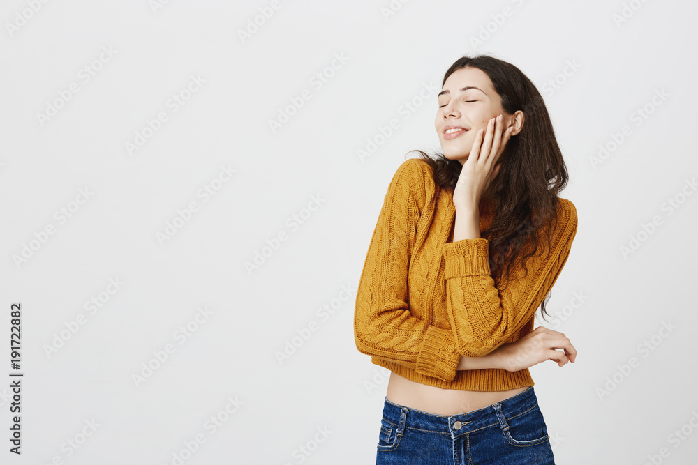 Studio portrait of attractive sensual dark-haired woman in flirting pose bending head backwards with closed eyes and seductive smile, holding hand on cheek, standing over gray background. Studio portrait of attractive sensual dark-haired woman in flirting pose bending head backwards with closed eyes and seductive smile, holding hand on cheek, standing over gray background.