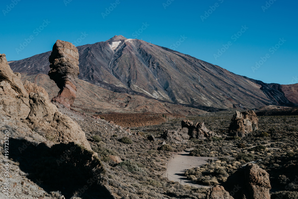 Teide Volcano with the clean blue sky on the background and rocks and trail on the front in the morning
