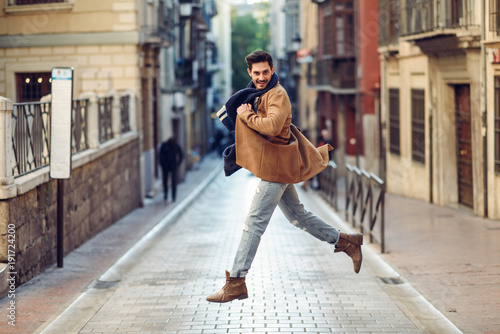 Young happy man jumping wearing winter clothes in urban background