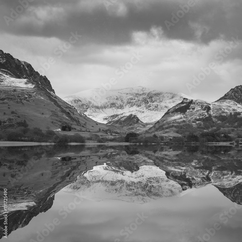 Beautiful black and white Winter landscape image of Llyn Nantlle in Snowdonia National Park with snow capped mountains in background