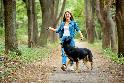 A young girl is walking with a German shepherd dog in the park.