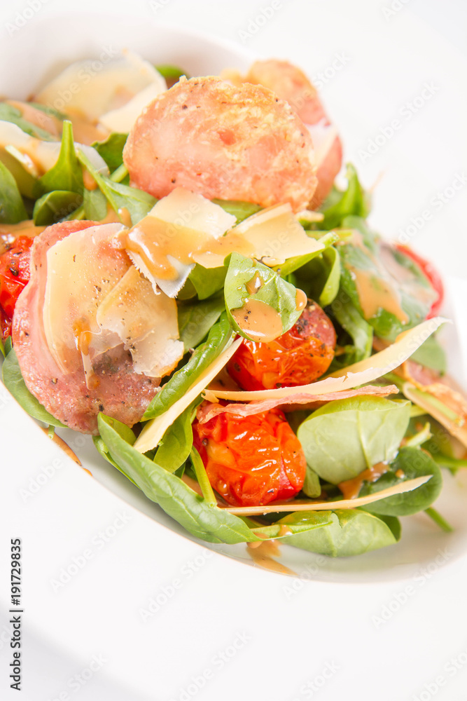 Baby spinach, dry sausage, matured cheese, roast tomatoes, thyme-balsamic vinaigrette salad on a white background Baby spinach, dry sausage, matured cheese, roast tomatoes, thyme-balsamic vinaigrette salad on a white background