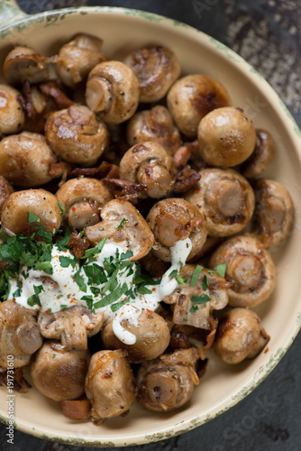 Above view of fried champignons and chanterelles with sour cream and parsley, close-up