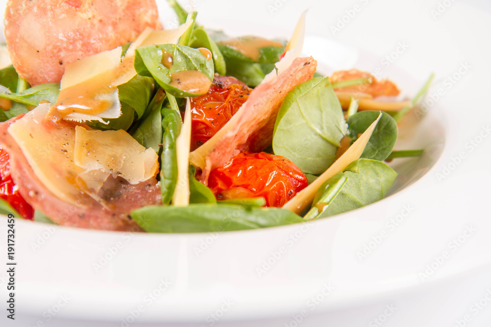 Baby spinach, dry sausage, matured cheese, roast tomatoes, thyme-balsamic vinaigrette salad on a white background Baby spinach, dry sausage, matured cheese, roast tomatoes, thyme-balsamic vinaigrette salad on a white background