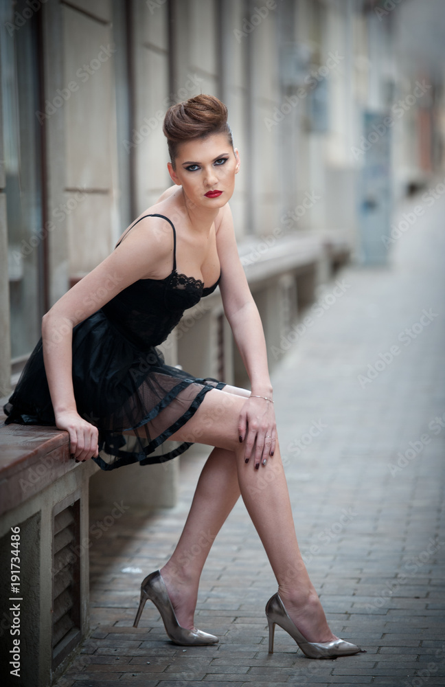 Sensual girl with long legs, short black dress and high heels sitting on  the bench.Handsome