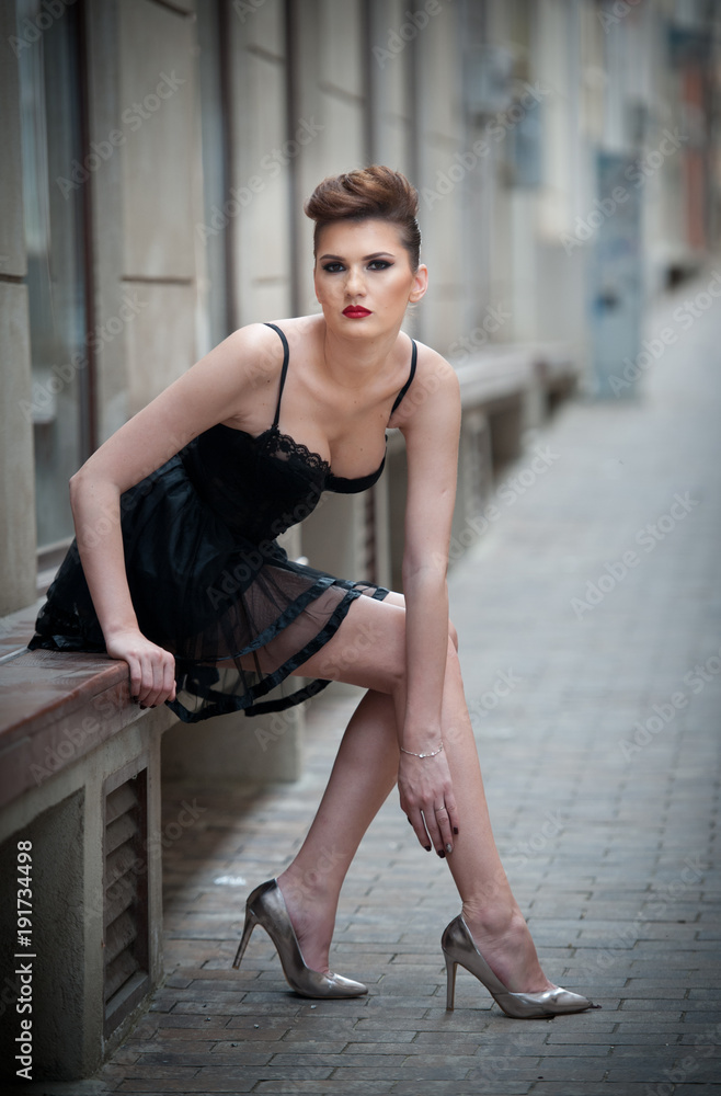 Sensual girl with long legs, short black dress and high heels sitting on  the bench.Handsome