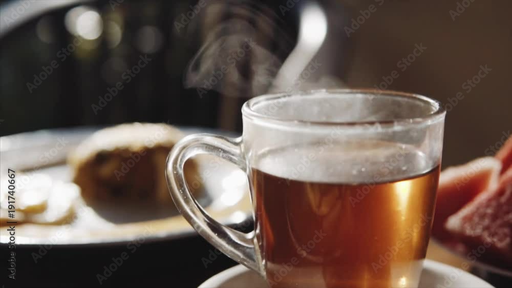 Transparent cup of hot black tea and breakfast on the blurred background on the wooden table , morning time Transparent cup of hot black tea and breakfast on the blurred background on the wooden table , morning time