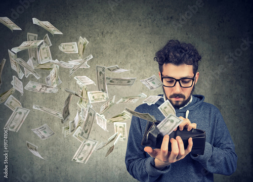 Hipster man looking at his wallet with money dollar banknotes flying out away photo