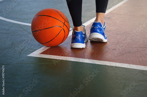 orange basketball on gymnasium floor with woman legs wear sport shoes for exercise