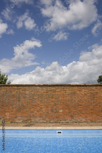 Old red brick wall contrasting with blue sky and swimming pool