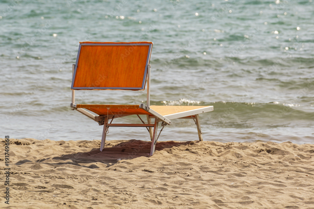 Bright chaise lounge on sand on seashore. Against background of sea Bright chaise lounge on sand on seashore. Against background of sea
