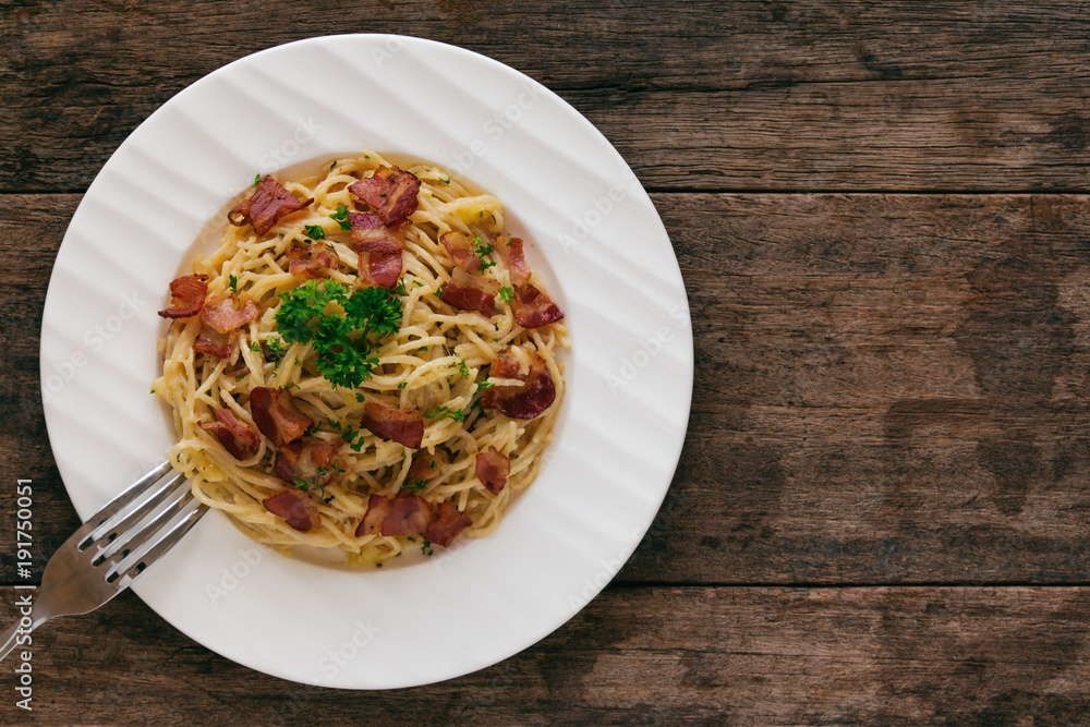 Spaghetti carbonara with bacon, cheese and chopped parsley on wood table in top view flat lay with copy space. Italian traditional homemade food for lunch or dinner so creamy and delicious. Spaghetti carbonara with bacon, cheese and chopped parsley on wood table in top view flat lay with copy space. Italian traditional homemade food for lunch or dinner so creamy and delicious.