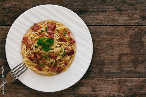 Spaghetti carbonara with bacon, cheese and chopped parsley on wood table in top view flat lay with copy space. Italian traditional homemade food for lunch or dinner so creamy and delicious.