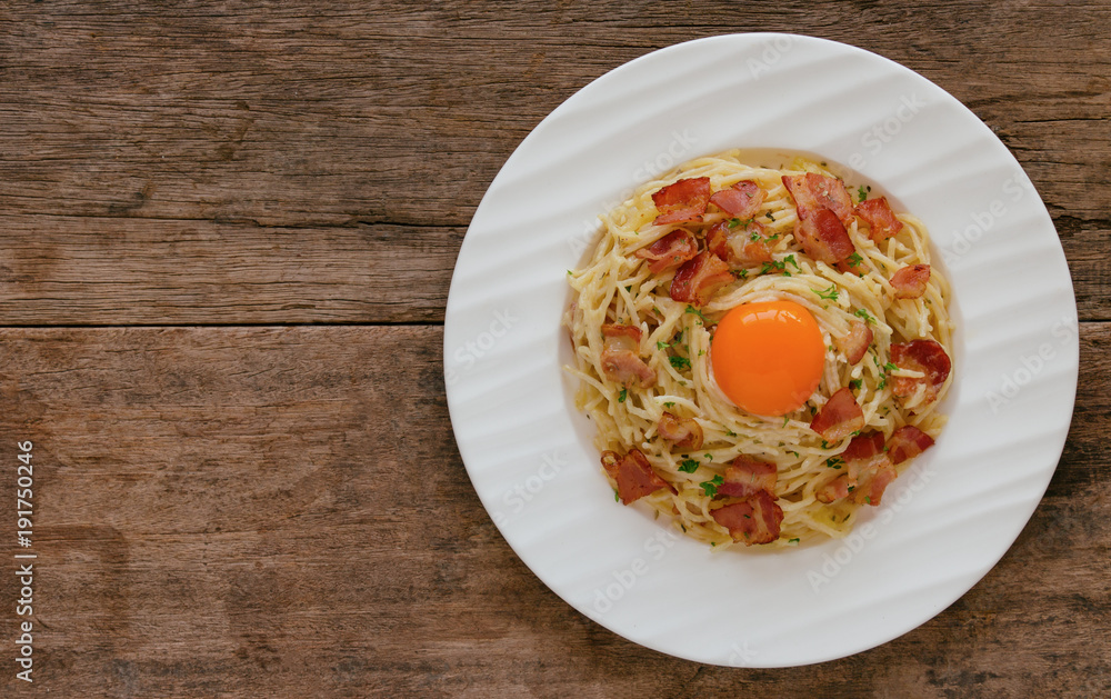Spaghetti carbonara with bacon, cheese, yolk and chopped parsley on wood table in top view flat lay with copy space. Italian traditional homemade food for lunch or dinner so creamy and delicious. Spaghetti carbonara with bacon, cheese, yolk and chopped parsley on wood table in top view flat lay with copy space. Italian traditional homemade food for lunch or dinner so creamy and delicious.
