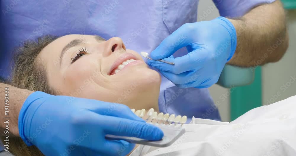 In a professional practice, a dentist checks the level of teeth whitening the patient's teeth with a dentist's color. Concept of: dentists, healthcare, perfection, white. In a professional practice, a dentist checks the level of teeth whitening the patient's teeth with a dentist's color. Concept of: dentists, healthcare, perfection, white.