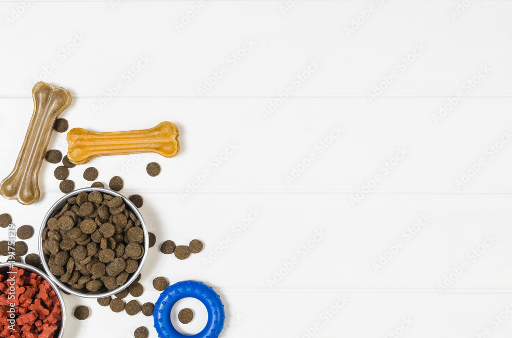Dry dog pet food in bowl and accessories on white wooden background top view. Pet feeding and care concept backgrounds with copy space. Photograph taken from above. Dry dog pet food in bowl and accessories on white wooden background top view. Pet feeding and care concept backgrounds with copy space. Photograph taken from above.