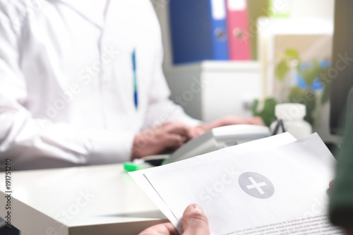 Medical results, report, document or record concept. Patient reading test or exam diagnosis paper or medicine prescription in doctor's office in hospital. Physician writing in the background.