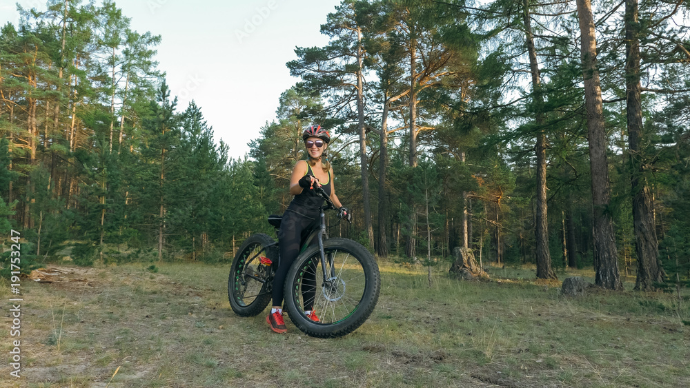 Fat bike also called fatbike or fat-tire bike in summer riding in the forest. Beautiful girl and her bicycle in the forest. She rolls her bike and poses to the operator.