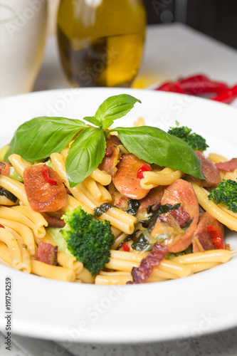 A delicious fresh gourmet Italian strozzapreti pasta dish, with pancetta, italian sausage, broccoli, vegetables, topped with fresh basil. photo