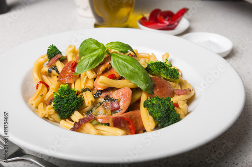 A delicious fresh gourmet Italian strozzapreti pasta dish, with pancetta, italian sausage, broccoli, vegetables, topped with fresh basil.